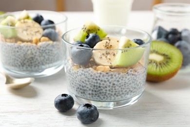 Photo of Delicious dessert with chia seeds, yogurt, granola, blueberries, banana and kiwi on white wooden table, closeup. Superfood