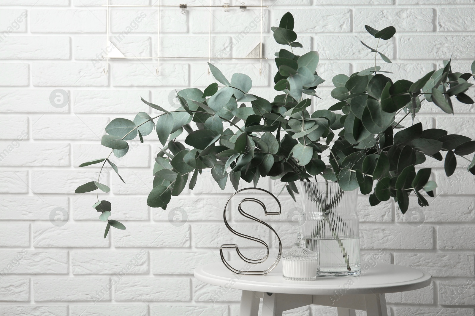 Green eucalyptus branches in vase and other decor on table near white brick wall indoors Photo of Green eucalyptus branches in vase and other decor on table near white brick wall indoors
