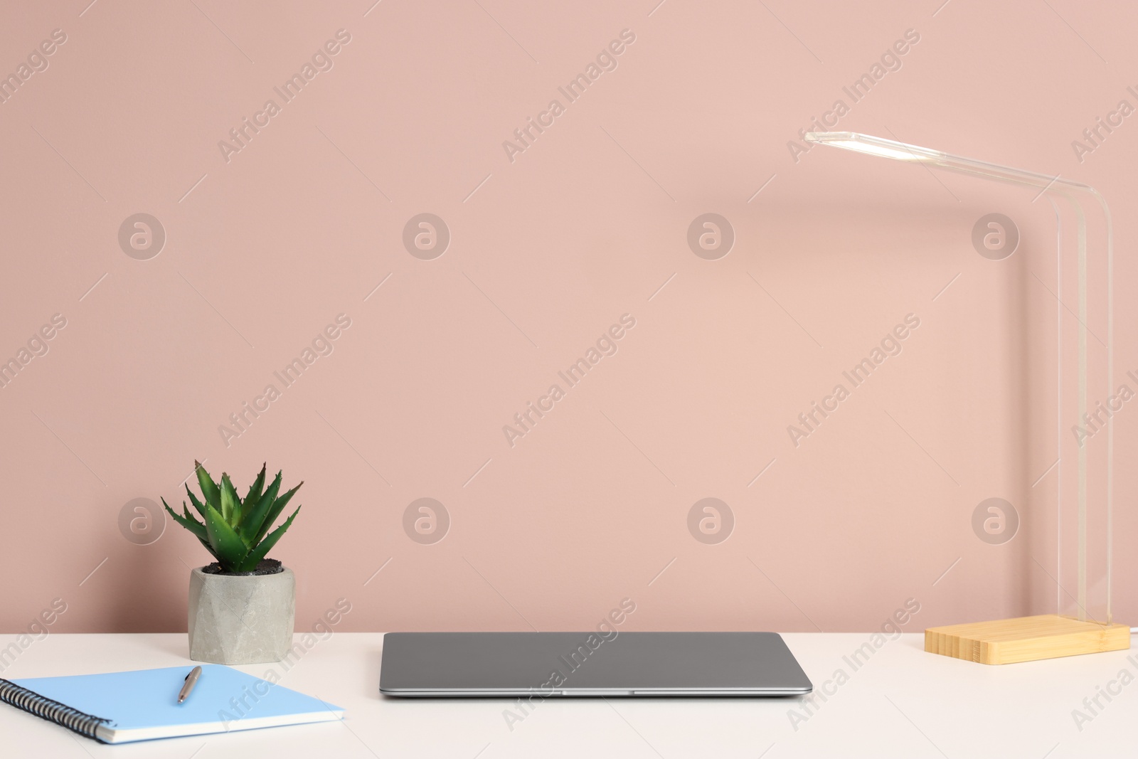 Laptop, stationery, lamp and floral decor on white office table against dark beige background Photo of Laptop, stationery, lamp and floral decor on white office table against dark beige background