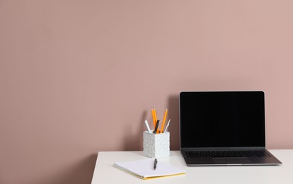 Photo of Laptop and different stationery on white office table against dark beige background, space for text