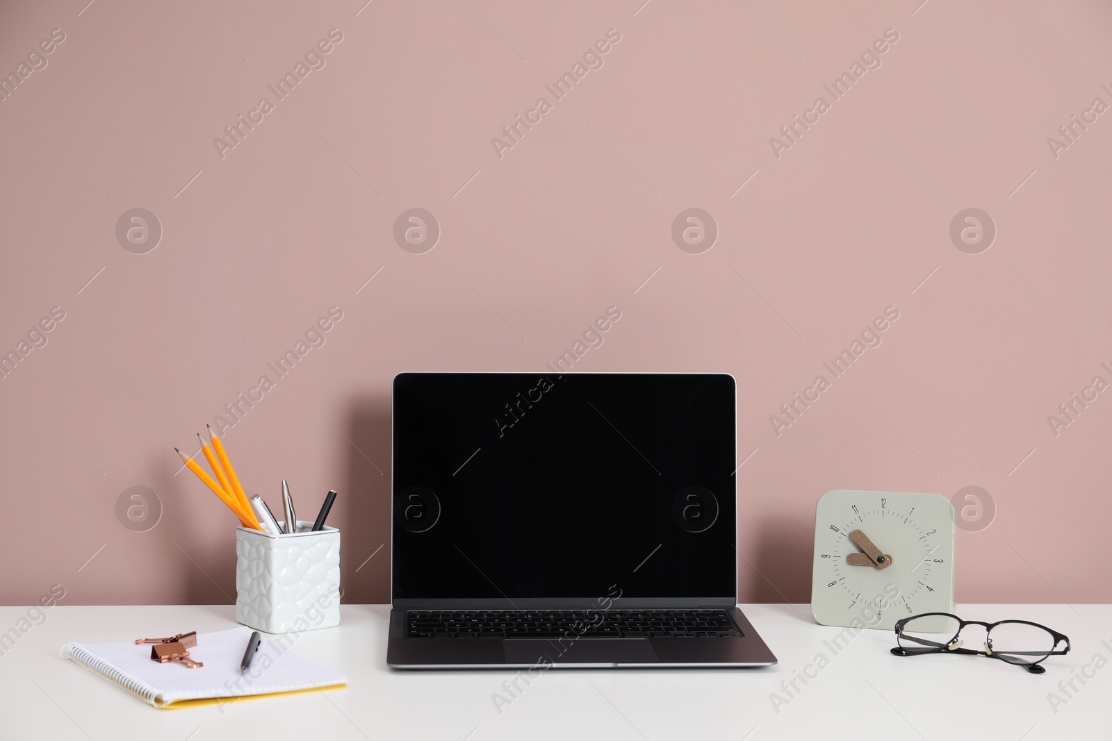 Laptop, different stationery, glasses and alarm clock on white office table against dark beige background Photo of Laptop, different stationery, glasses and alarm clock on white office table against dark beige background
