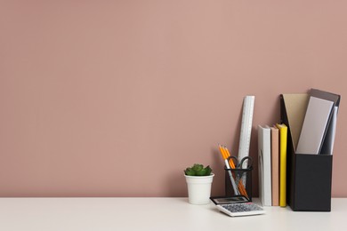 Photo of Different stationery, floral decor and calculator on white office table against dark beige background, space for text