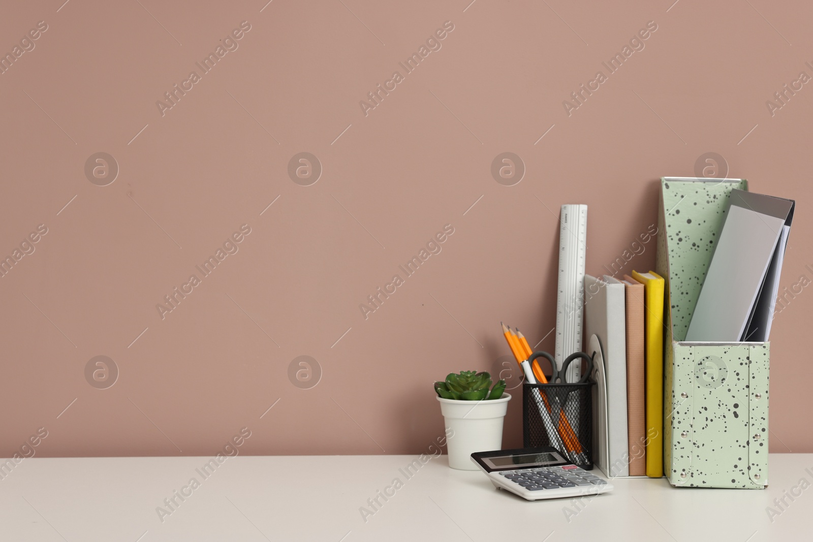 Different stationery, floral decor and calculator on white office table against dark beige background, space for text Photo of Different stationery, floral decor and calculator on white office table against dark beige background, space for text