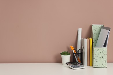 Photo of Different stationery, floral decor and calculator on white office table against dark beige background, space for text
