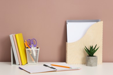 Photo of Different stationery and floral decor on white office table against dark beige background