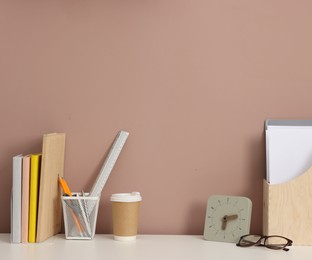 Photo of Different stationery, glasses and alarm clock on white office table against dark beige background