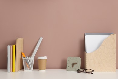 Photo of Different stationery, glasses and alarm clock on white office table against dark beige background