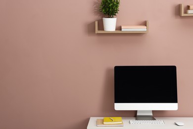 Photo of Computer, keyboard, mouse and different stationery on white office table near dark beige wall, space for text