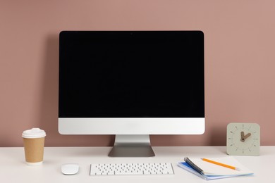 Photo of Computer, keyboard, mouse, coffee, alarm clock and different stationery on white office table against dark beige background