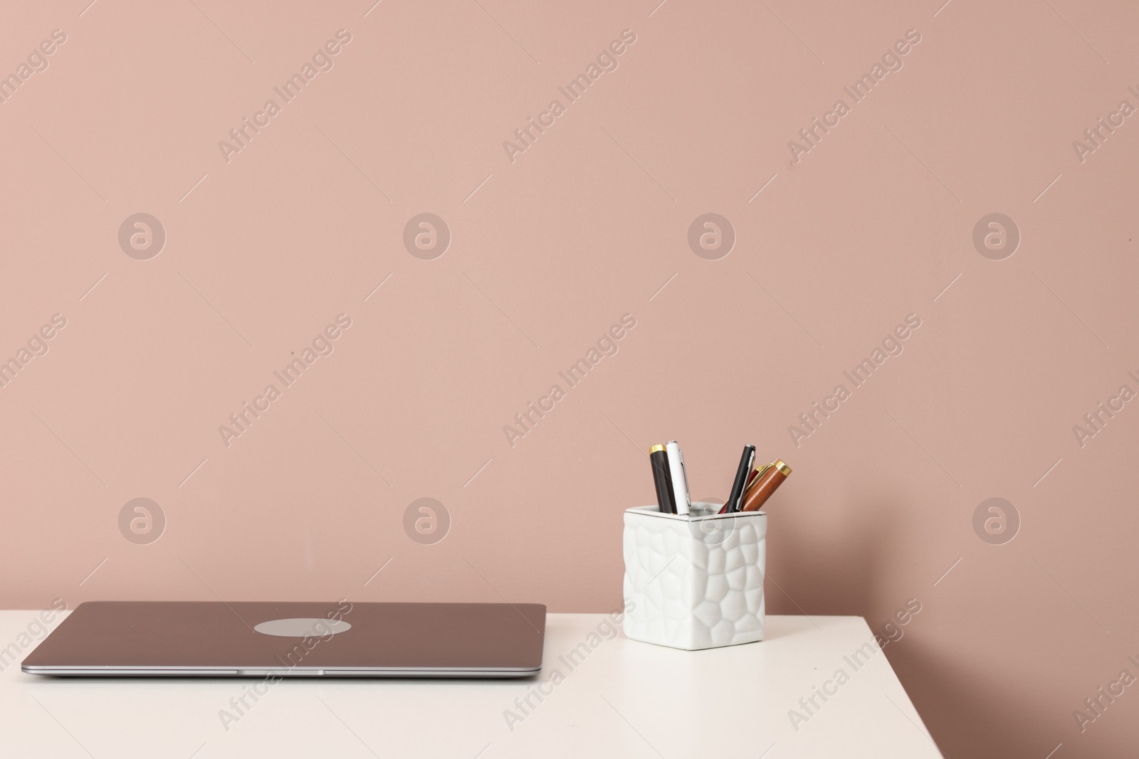 Laptop and different stationery on white office table against dark beige background Photo of Laptop and different stationery on white office table against dark beige background