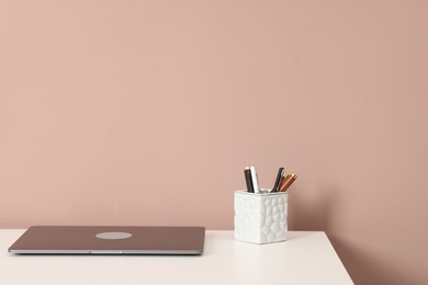 Photo of Laptop and different stationery on white office table against dark beige background