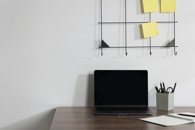 Photo of Laptop and different stationery on wooden office table near white wall, space for text