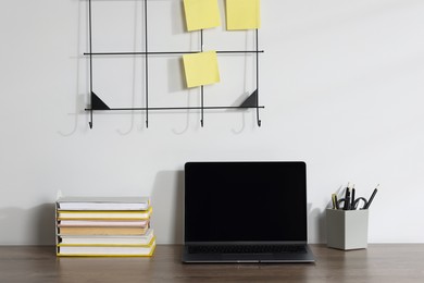 Photo of Laptop and different stationery on wooden office table near white wall