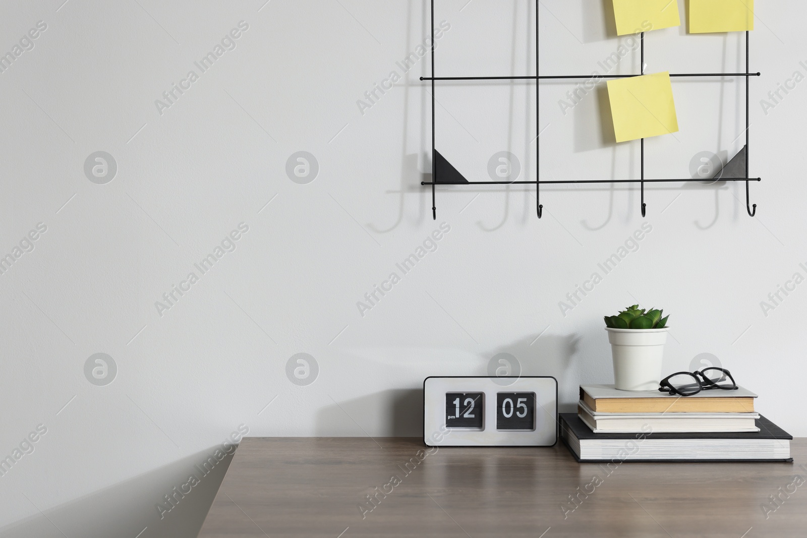 Stationery, flip clock, floral decor and glasses on wooden office table near white wall Photo of Stationery, flip clock, floral decor and glasses on wooden office table near white wall
