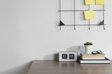 Photo of Stationery, flip clock, floral decor and glasses on wooden office table near white wall
