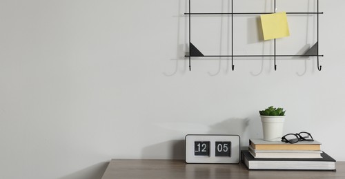 Photo of Stationery, flip clock, floral decor and glasses on wooden office table near white wall