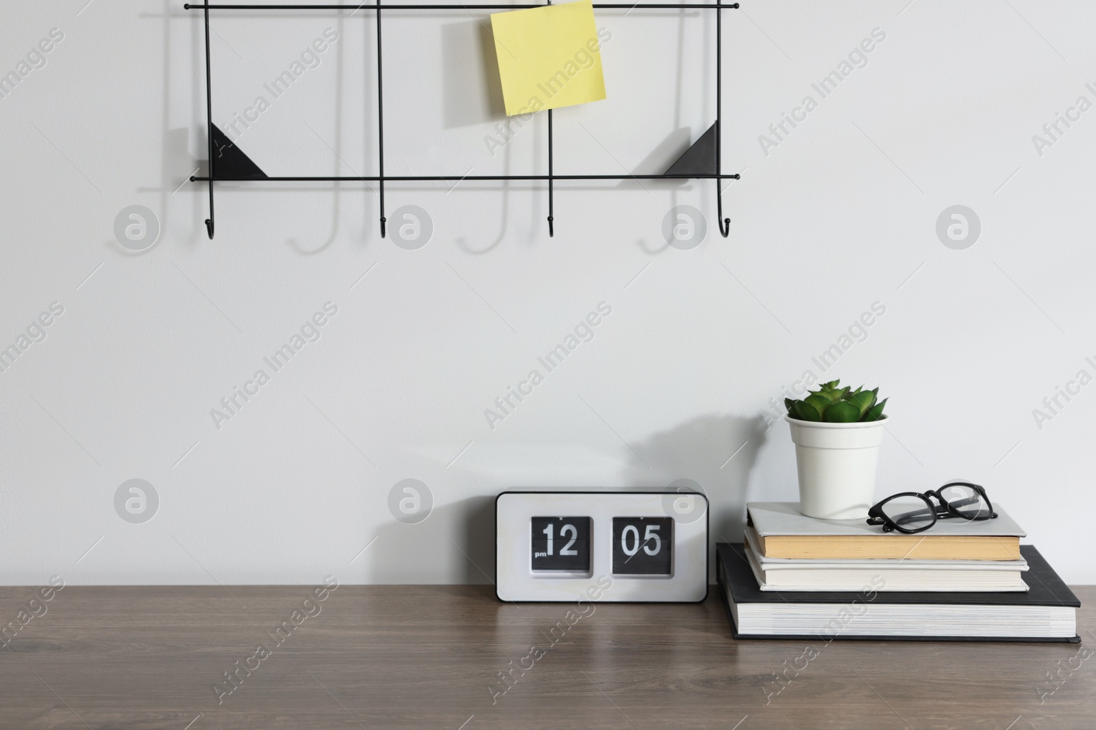 Stationery, flip clock, floral decor and glasses on wooden office table near white wall Photo of Stationery, flip clock, floral decor and glasses on wooden office table near white wall