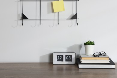 Photo of Stationery, flip clock, floral decor and glasses on wooden office table near white wall