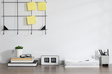 Photo of Stationery, flip clock, floral decor and glasses on wooden office table near white wall