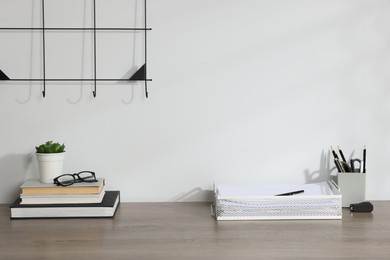 Photo of Different stationery, floral decor and glasses on wooden office table near white wall