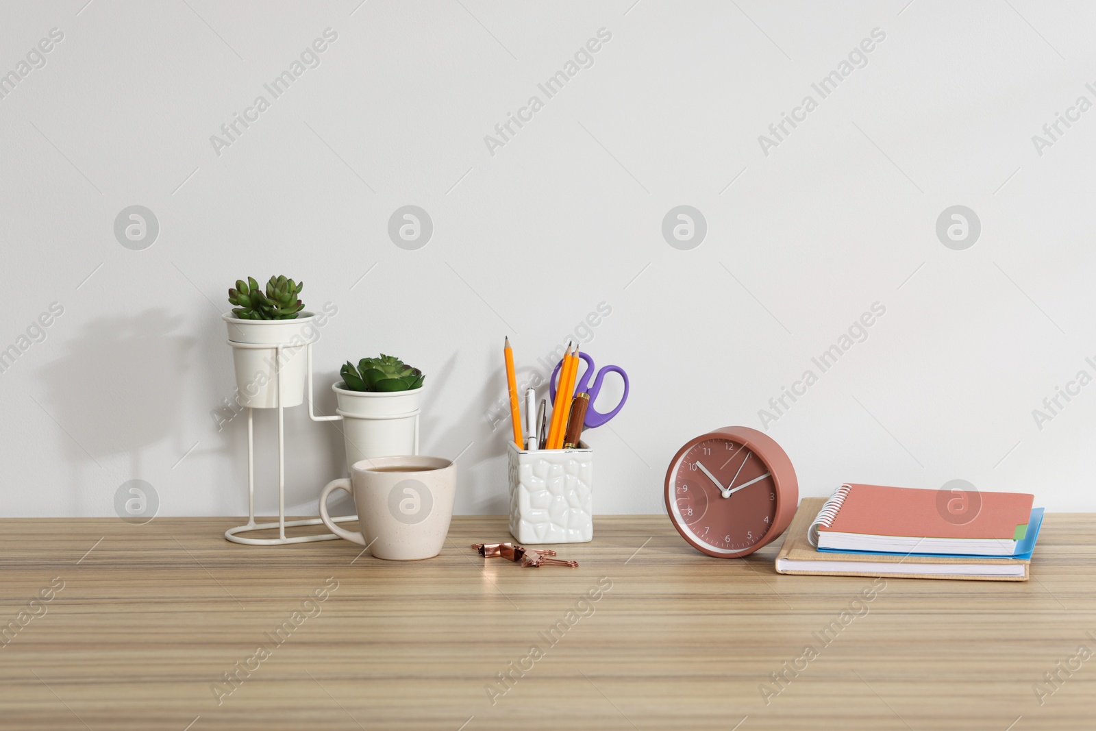 Different stationery, floral decor, alarm clock and coffee on wooden office table against white background Photo of Different stationery, floral decor, alarm clock and coffee on wooden office table against white background