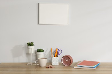 Photo of Different stationery, floral decor, alarm clock and coffee on wooden office table near white wall
