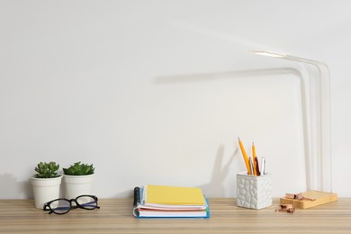 Photo of Different stationery, floral decor, glasses and lamp on wooden office table against white background