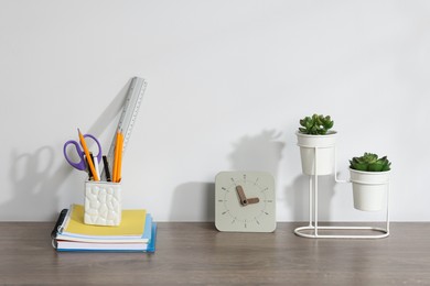 Photo of Different stationery, floral decor and alarm clock on wooden office table against white background