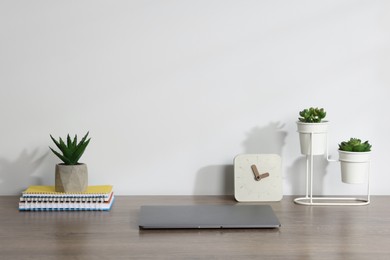 Photo of Laptop, stationery, floral decor and alarm clock on wooden office table against white background