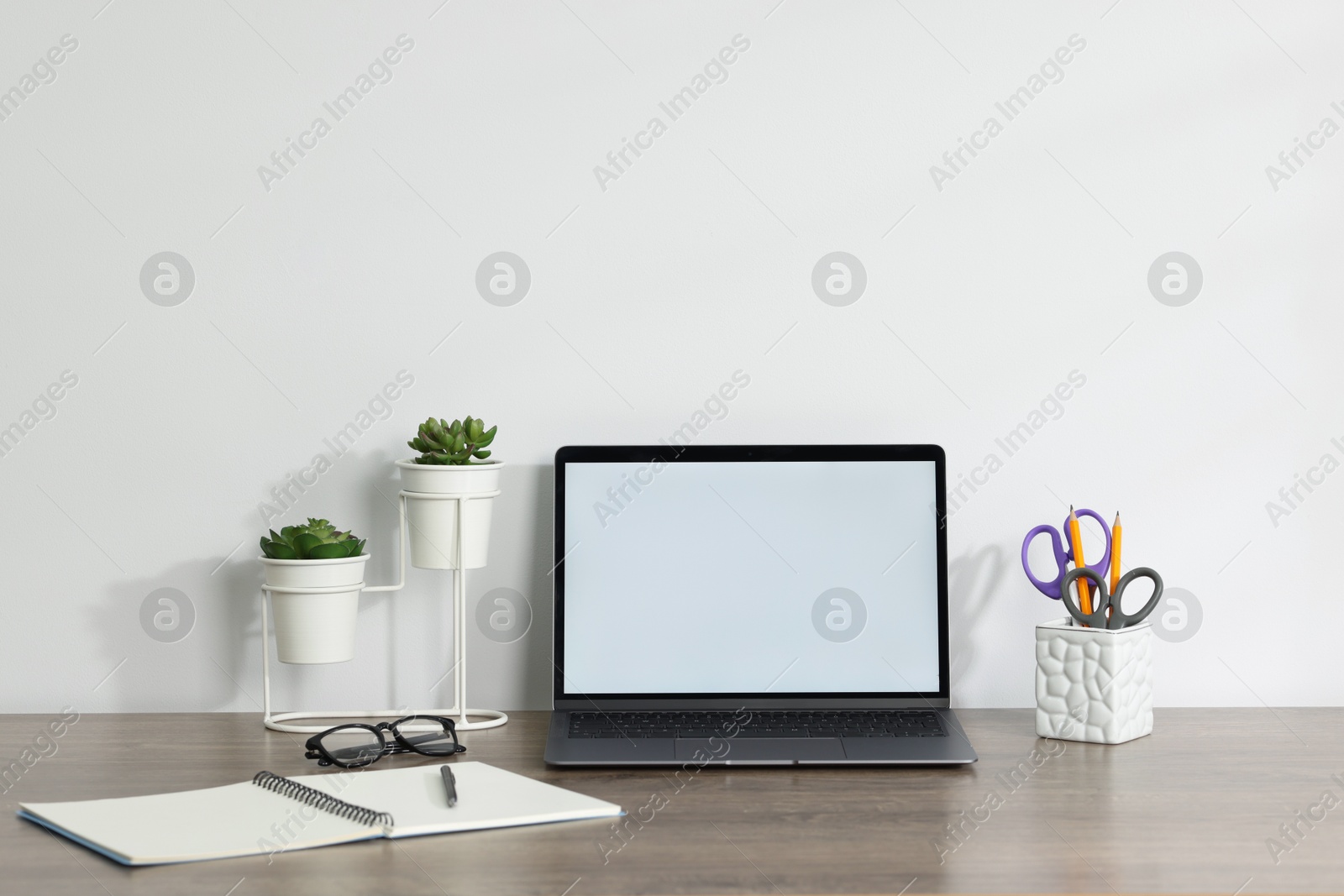 Laptop, different stationery, glasses and floral decor on wooden office table against white background Photo of Laptop, different stationery, glasses and floral decor on wooden office table against white background