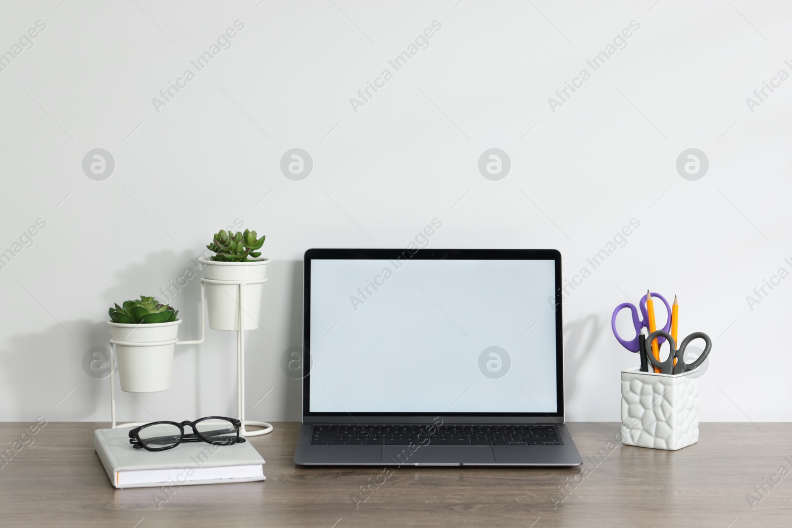 Laptop, different stationery, glasses and floral decor on wooden office table against white background Photo of Laptop, different stationery, glasses and floral decor on wooden office table against white background