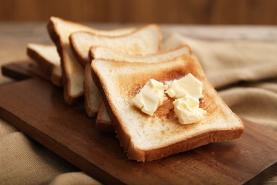 Photo of Crispy toasts with butter on wooden board, closeup