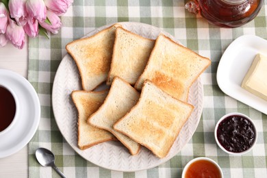 Photo of Tasty crispy toasted bread slices, tea, butter and jam on table, flat lay