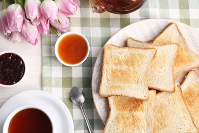 Photo of Tasty crispy toasted bread slices, tea and jam on table, flat lay