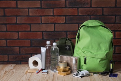 Photo of Survival kit. Different emergency supplies on wooden table against brick wall, space for text