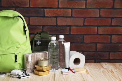 Photo of Survival kit. Different emergency supplies on wooden table against brick wall, space for text