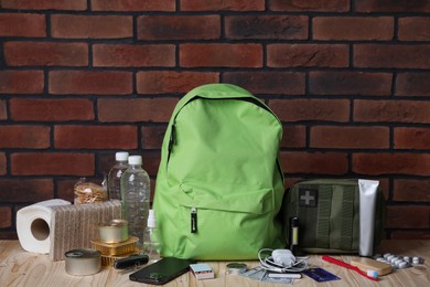 Photo of Survival kit. Different emergency supplies on wooden table against brick wall