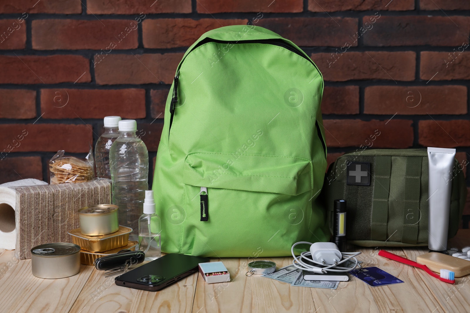 Survival kit. Different emergency supplies on wooden table against brick wall Photo of Survival kit. Different emergency supplies on wooden table against brick wall