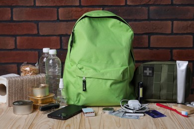 Photo of Survival kit. Different emergency supplies on wooden table against brick wall