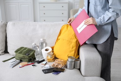 Photo of Survival kit. Woman putting documents into backpack indoors, closeup