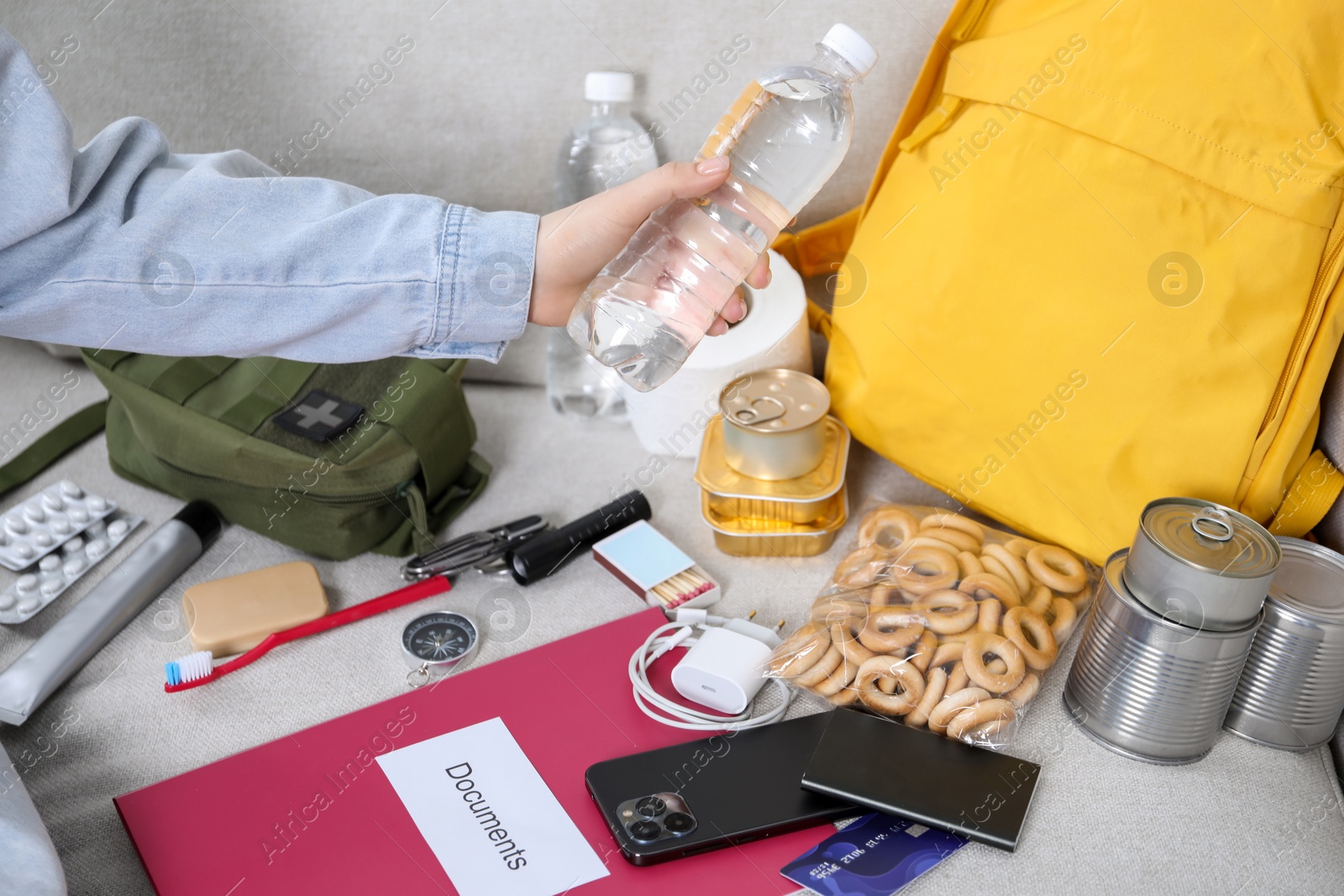 Survival kit. Woman packing different emergency supplies on sofa indoors, closeup Photo of Survival kit. Woman packing different emergency supplies on sofa indoors, closeup