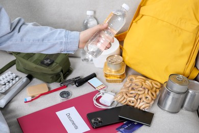 Photo of Survival kit. Woman packing different emergency supplies on sofa indoors, closeup