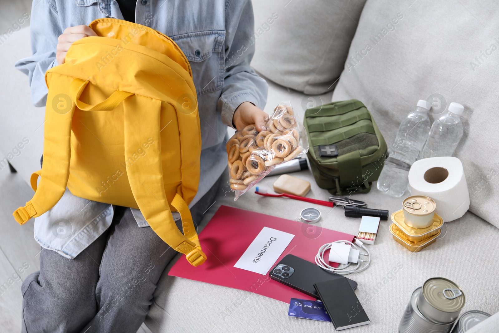 Survival kit. Woman packing different emergency supplies on sofa indoors, closeup Photo of Survival kit. Woman packing different emergency supplies on sofa indoors, closeup