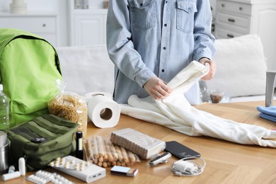 Photo of Survival kit. Woman packing different emergency supplies at wooden table indoors, closeup