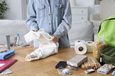 Photo of Survival kit. Woman packing different emergency supplies at wooden table indoors, closeup