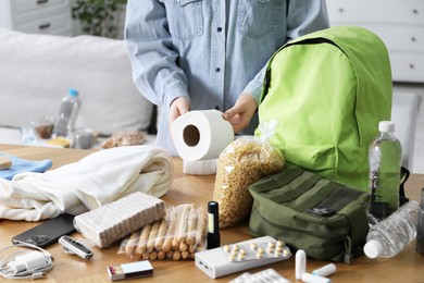 Photo of Survival kit. Woman packing different emergency supplies at wooden table indoors, closeup