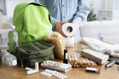 Photo of Survival kit. Woman packing different emergency supplies at wooden table indoors, closeup