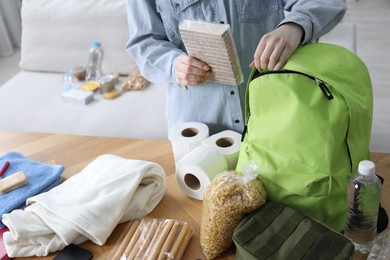 Photo of Survival kit. Woman packing different emergency supplies at wooden table indoors, closeup