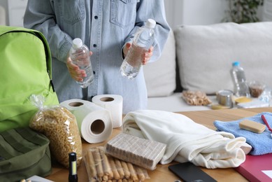 Photo of Survival kit. Woman packing different emergency supplies at wooden table indoors, closeup