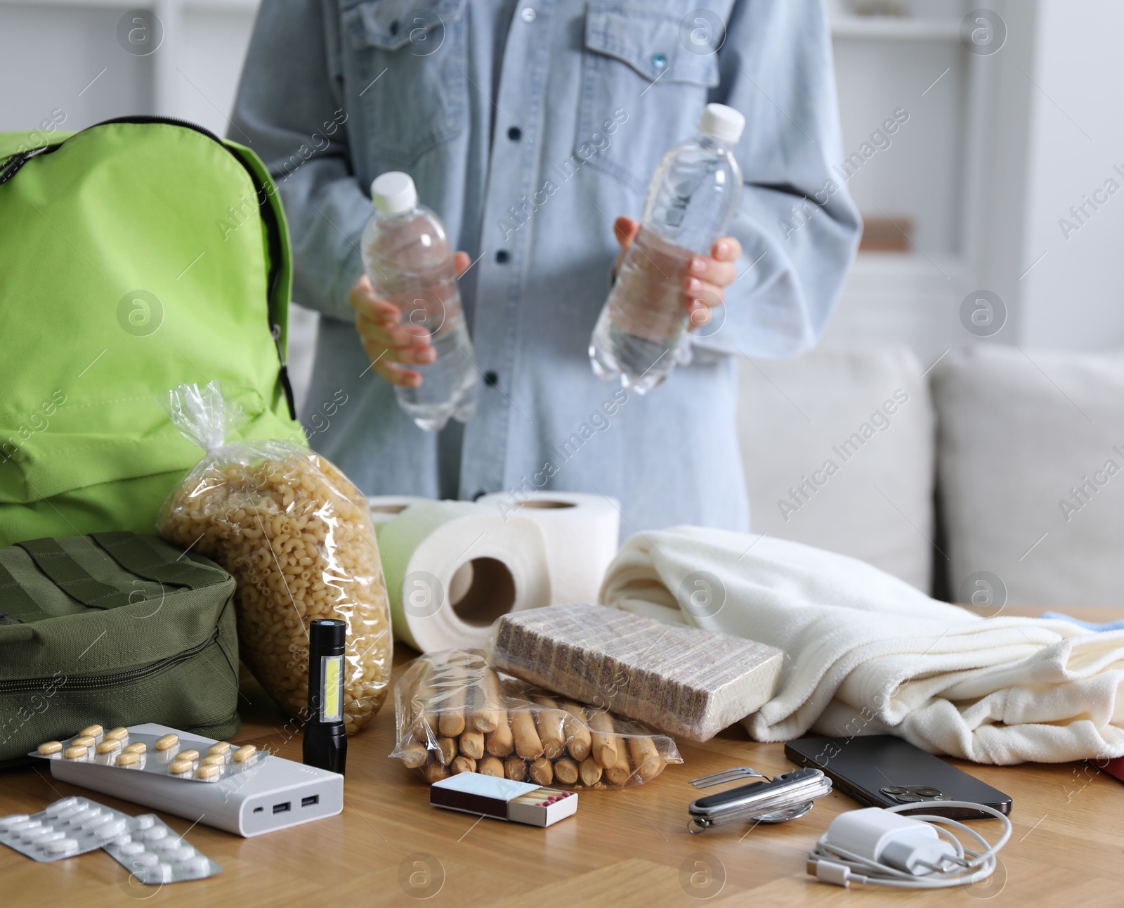 Survival kit. Woman packing different emergency supplies at wooden table indoors, closeup Photo of Survival kit. Woman packing different emergency supplies at wooden table indoors, closeup